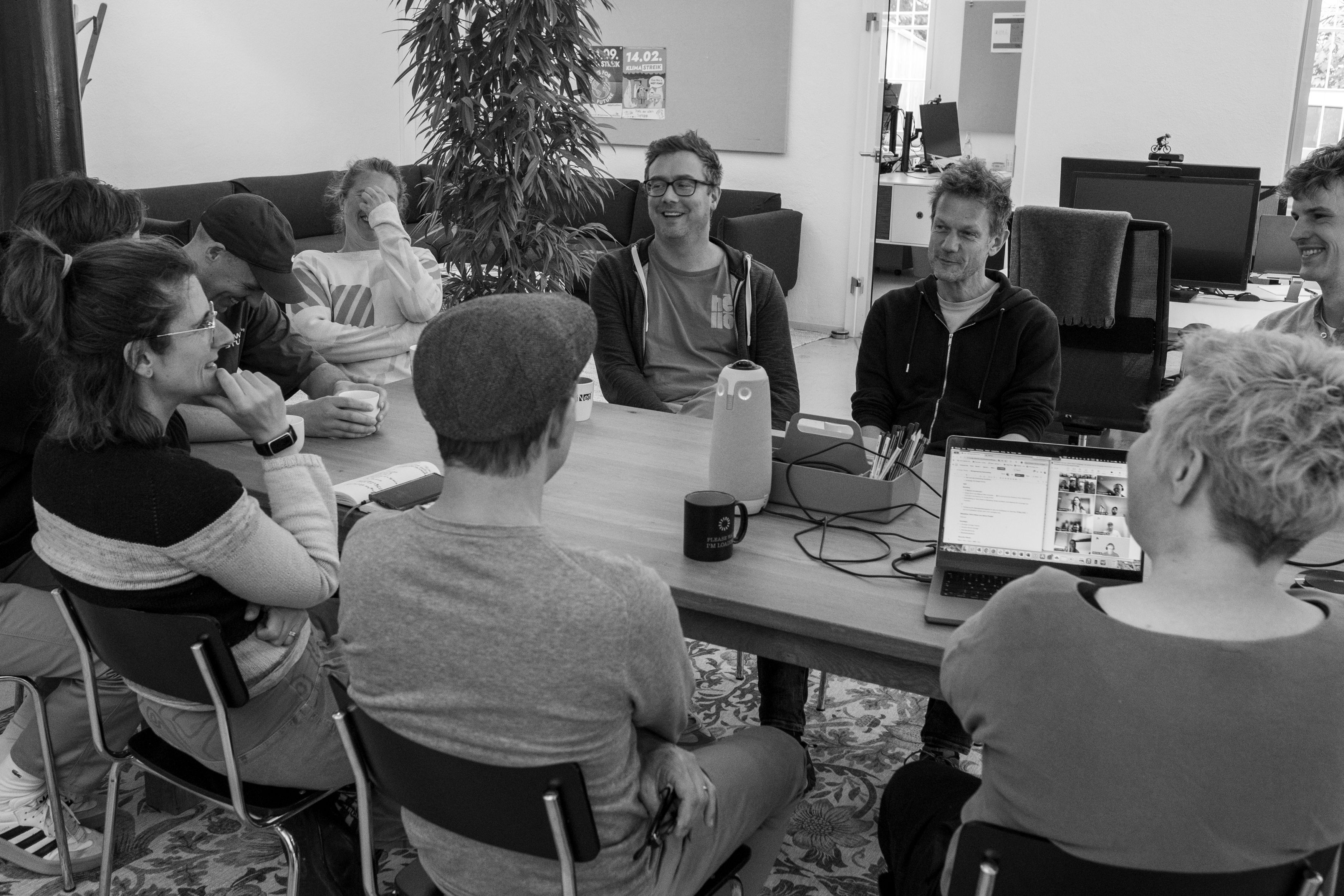 re-lounge-Team an großem Tisch bei einem fröhlichen Meeting - einige Personen auf dem Bild lachen oder lächeln